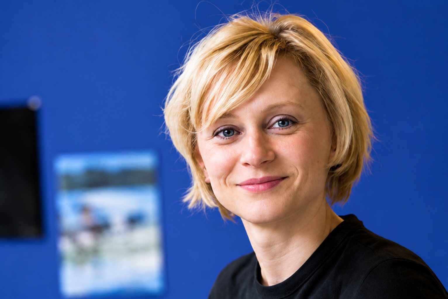 Femme blonde souriante sur fond bleu, portrait de bureau