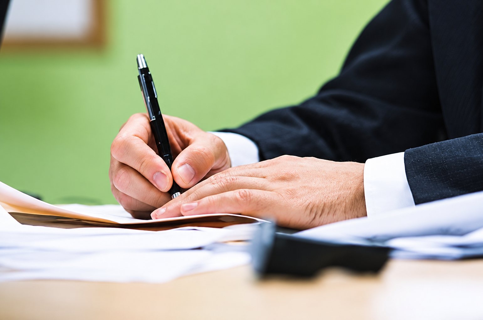 Main qui signe un document, manches de costume sombre, fond vert